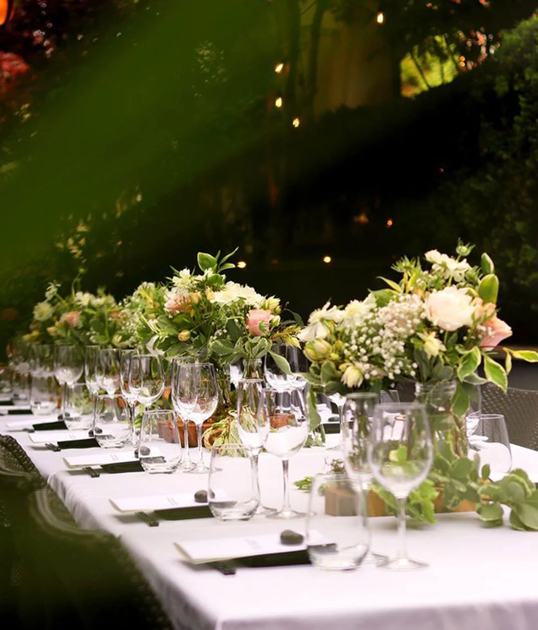 Elegant outdoor dining table setting with floral centerpieces.