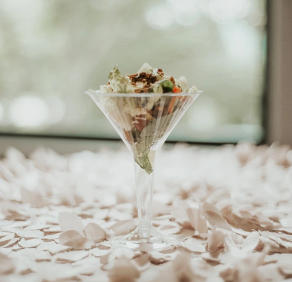 Martini glass filled with salad on petal-covered table.