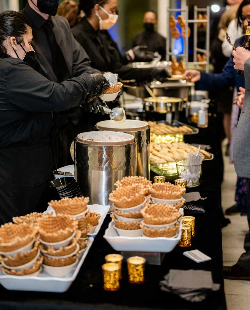 Catering staff serving ice cream at event buffet table.