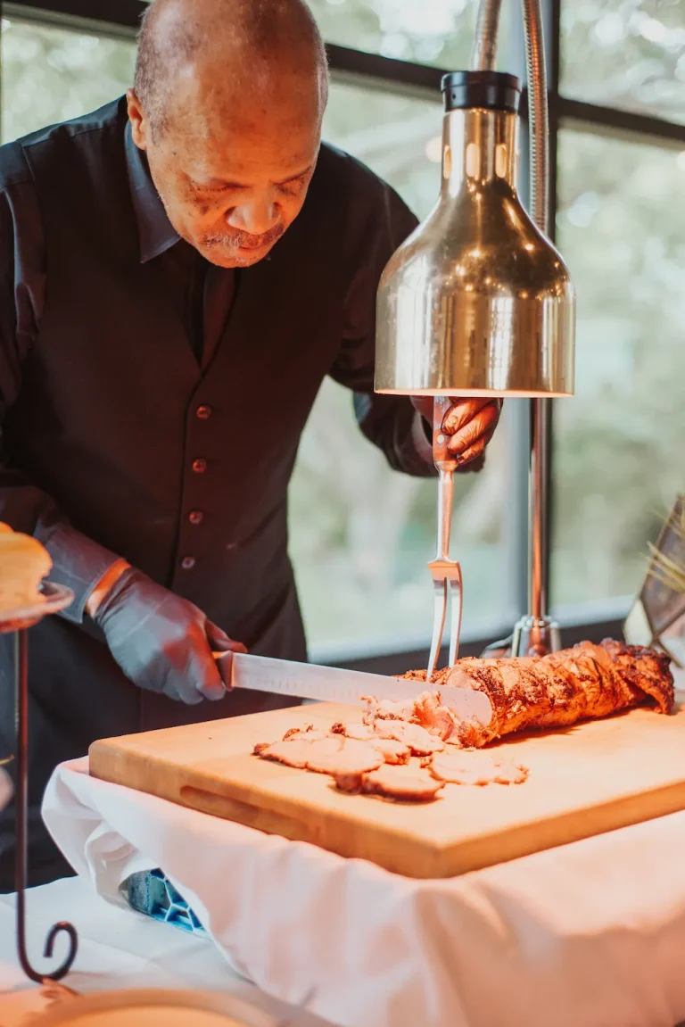 Chef carving roasted meat under heat lamp