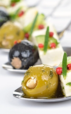 Gourmet olives and cheese appetizers on spoons.